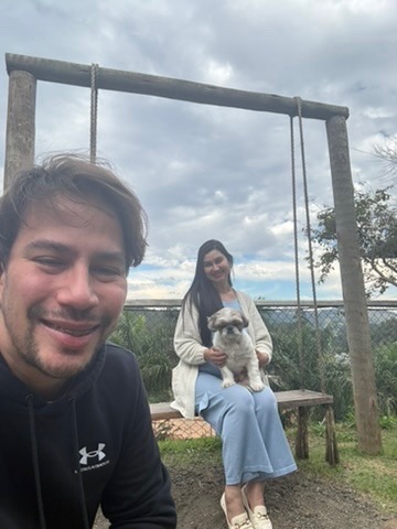 Bruno em primeiro plano e Luciana em um balanço com o cachorro no colo